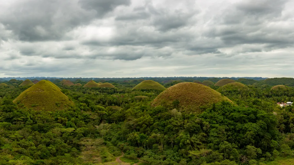 Rozsáhlé panorama Čokoládových kopců (Chocolate Hills) na Boholu s dramatickými mraky na obloze. Zelené kopce vytvářejí jedinečný přírodní úkaz, který je jednou z nejznámějších turistických atrakcí Filipín.