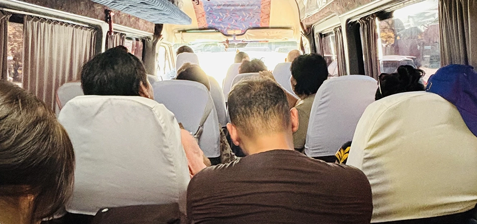 Pohled zezadu na interiér přeplněného minibusu v Kyrgyzstánu. Cestující sedí natlačení, někteří sledují své telefony. Strop a stěny autobusu jsou zdobené typickými vzory, jež se často vyskytují v místních dopravních prostředcích ve Střední Asii.