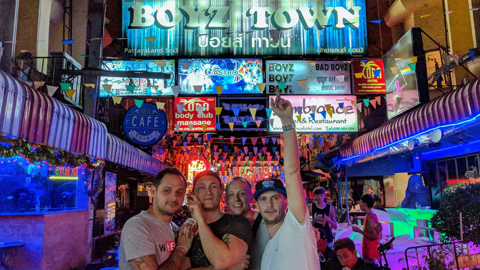 Peter Zošiak se třemi kamarády pózuje v živé noční ulici Pattayi pod neonovým nápisem „BOYZ TOWN“. Barevná světla, bary a noční atmosféra města.