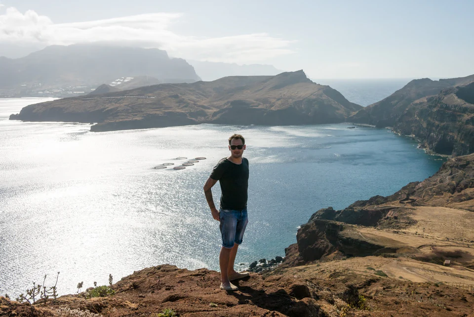 Peter Zošiak stojí na útesech s výhledem na modrý oceán a skalnaté pobřeží na ostrove Madeira. Slunce odrážející se na vodní hladině vytváří dramatickou scenérii.