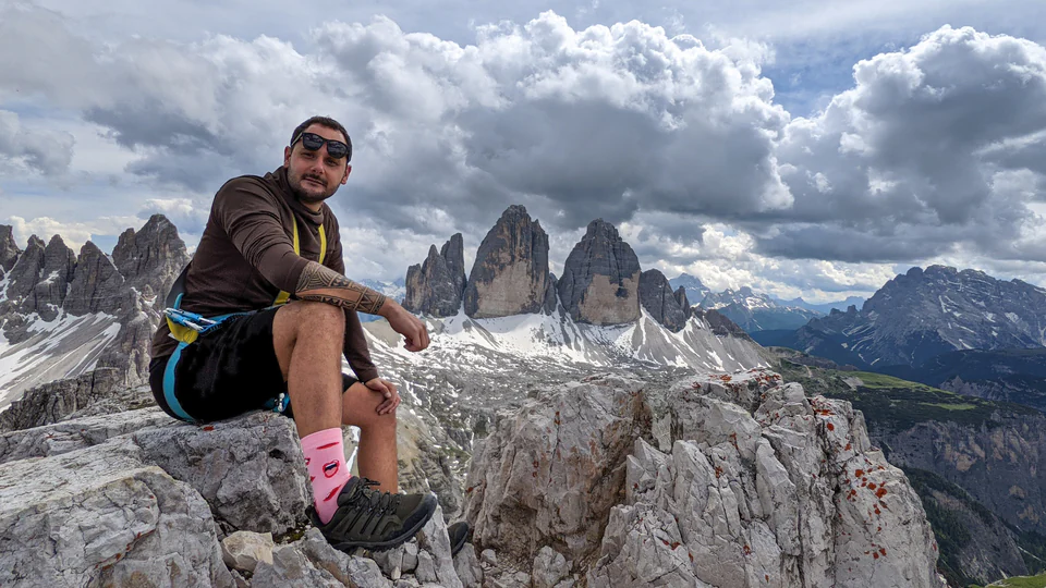Peter Zošiak sedí na skalním vrcholu s výhledem na majestátní Dolomity v Italii. Okolo dramatické horské scenérie s hustými mraky a sněhem pokrytými vrcholy.